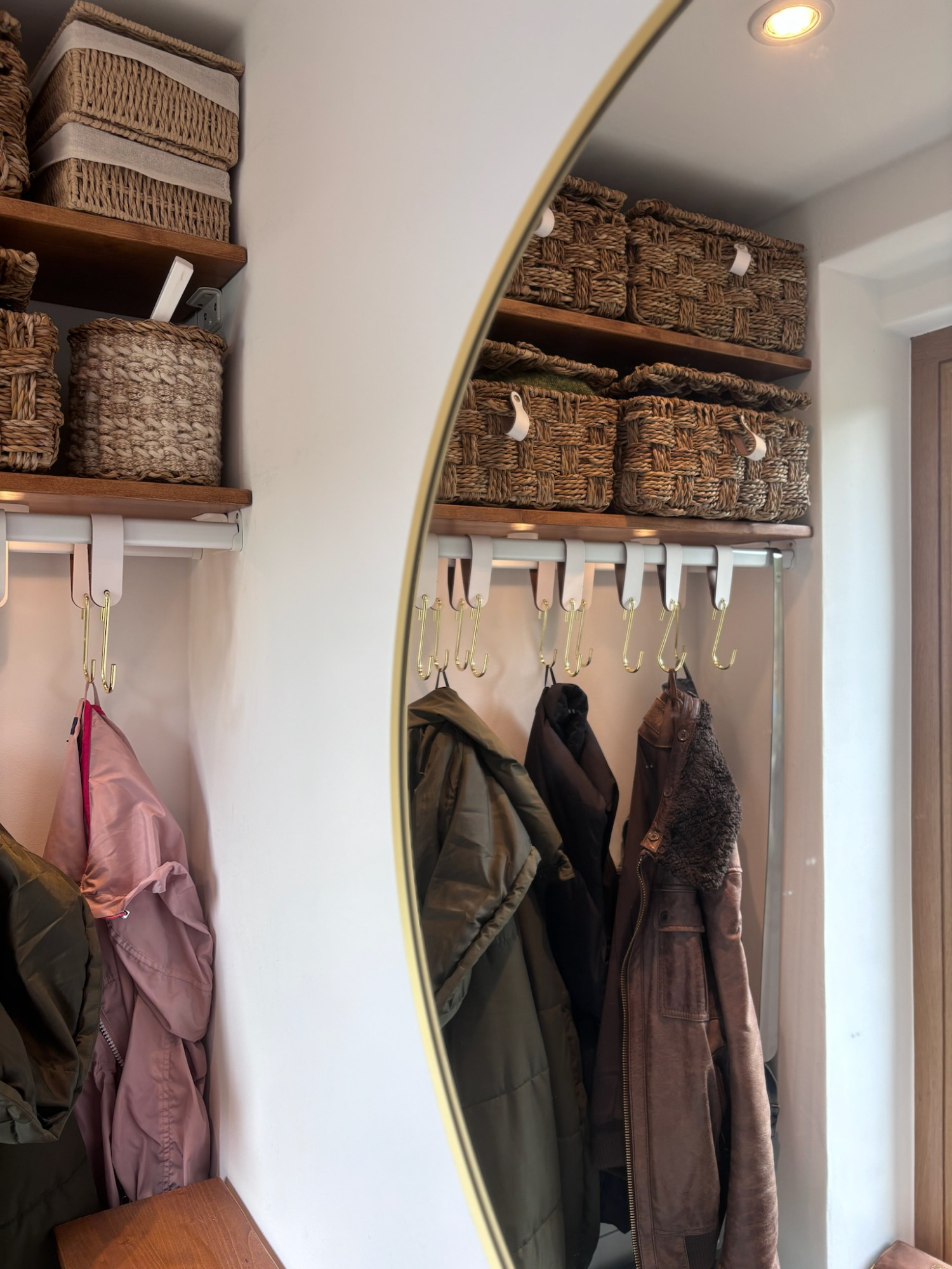 Garderobe - Projekt H9 Runder Spiegel an einer Wand mit Aufbewahrungskörben und aufgehängten Jacken.